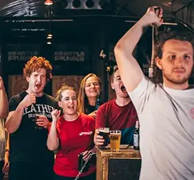 Man throwing an axe while a group of people cheer on behind