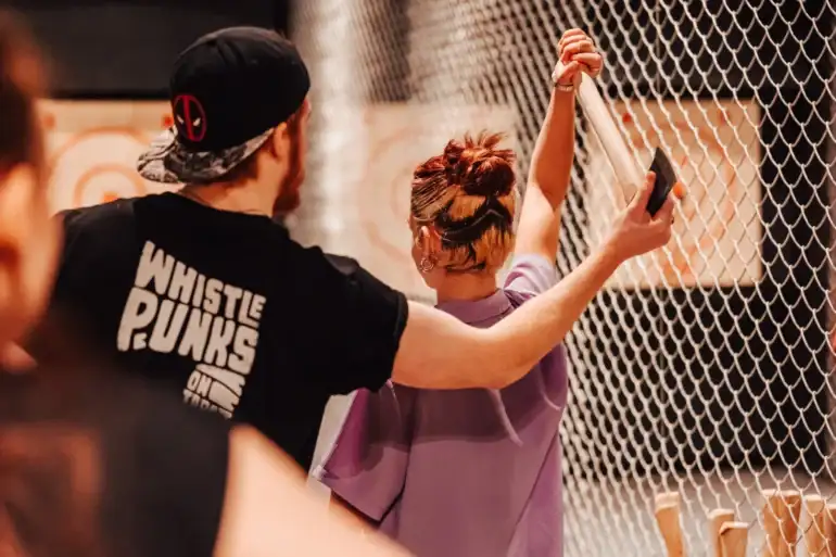 A person throwing an axe with an instructor teaching them the correct stance and technique.